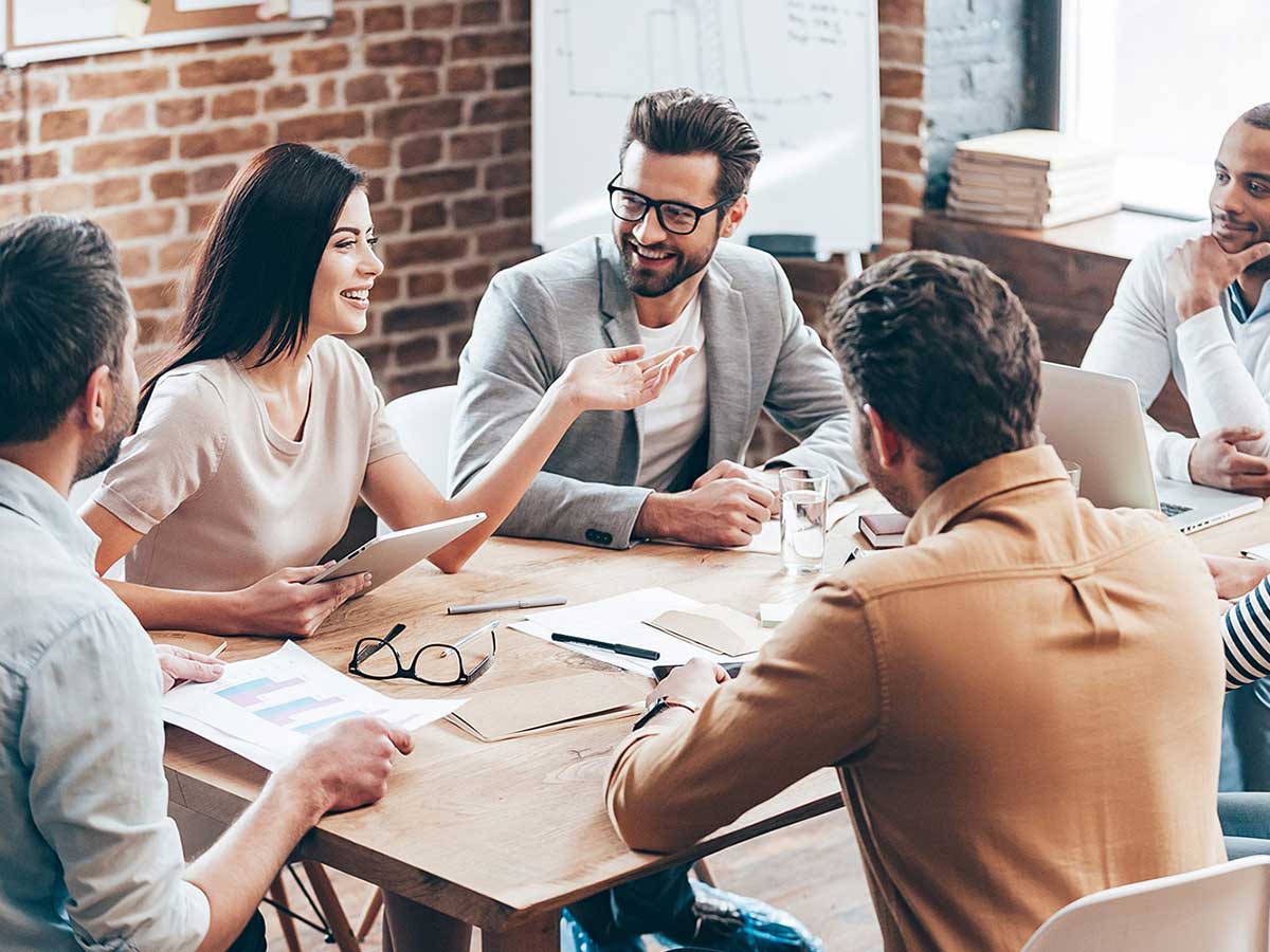 Group of professional people sitting at a big desk and talking to each other.